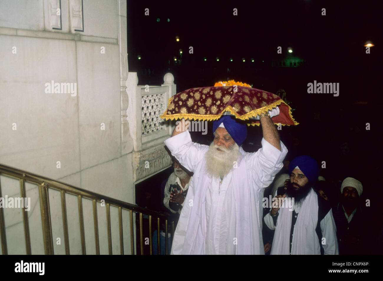 La religione sikh uomo che porta sulla sua testa il Guru Granth Sahib, il libro sacro dei sikh. Tempio d'oro, Amritsar Foto Stock