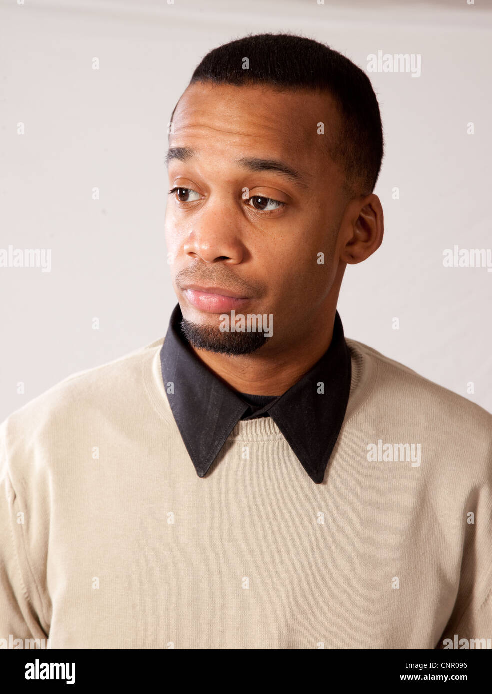 Considerato giovane uomo nero, che indossa un maglione e guardando tutti pensieroso e triste Foto Stock