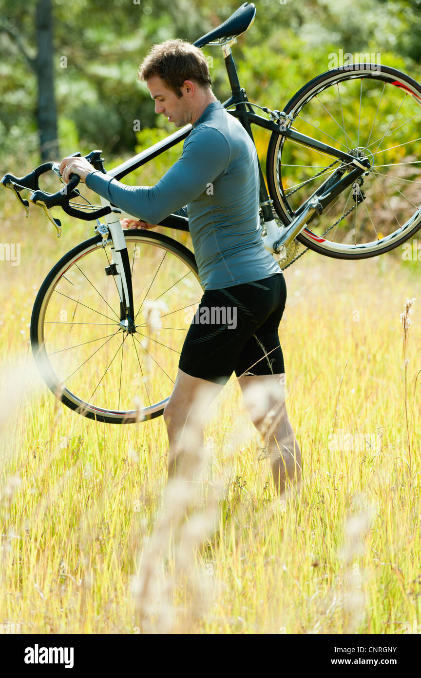 Uomo che porta bicicletta sulla spalla, camminando attraverso l'erba Foto  stock - Alamy