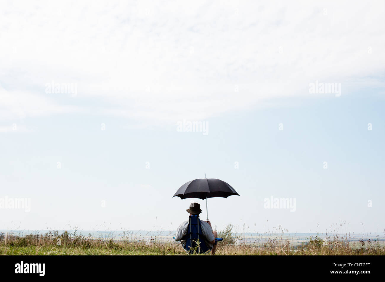 Uomo seduto sotto ombrellone in campo Foto Stock