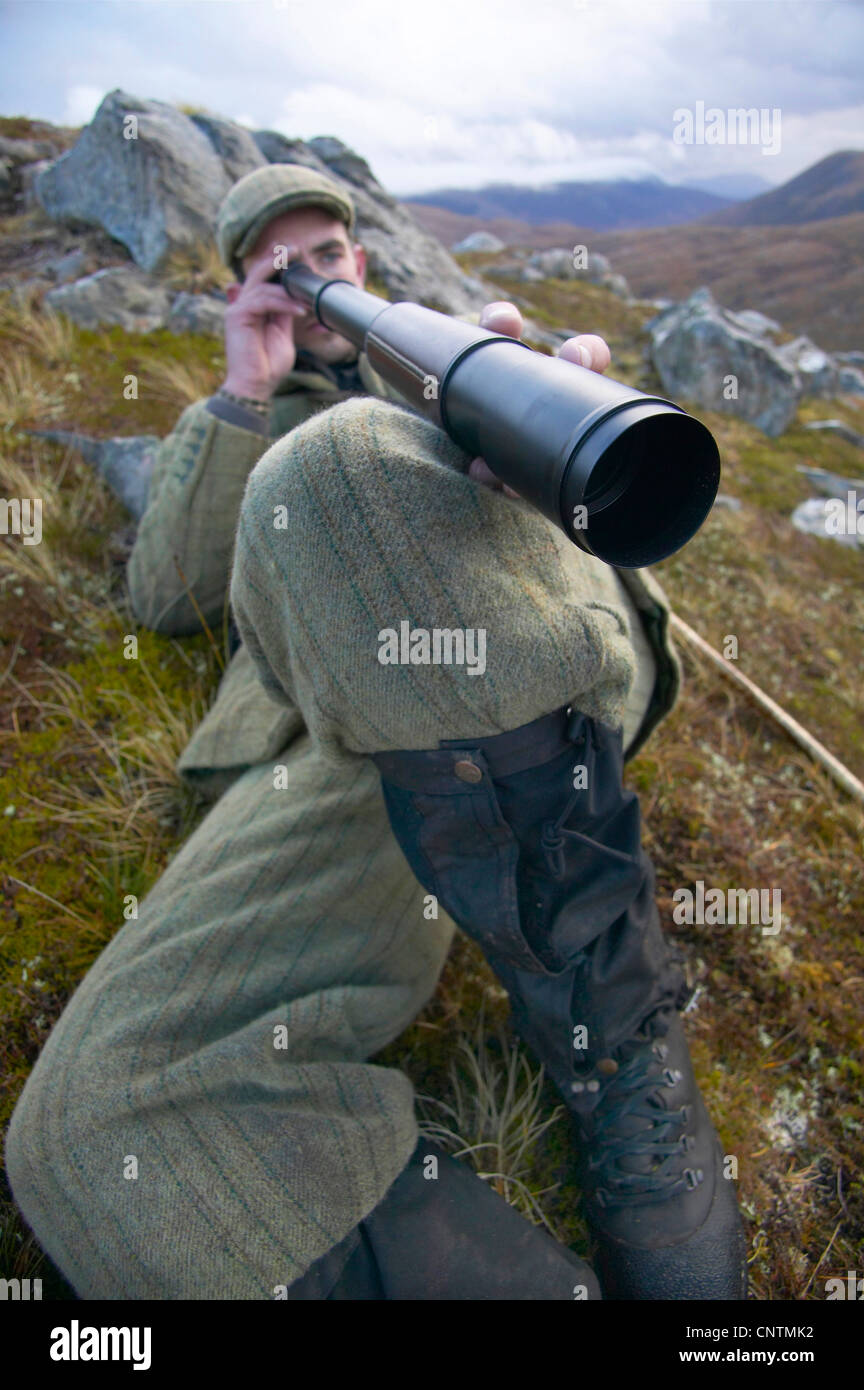 Stalker giacente in erba su un pendio di montagna guardando in giù in una valle fluviale attraverso un telescopio, Regno Unito, Scozia, Sutherland, Alladale deserto riserva Foto Stock