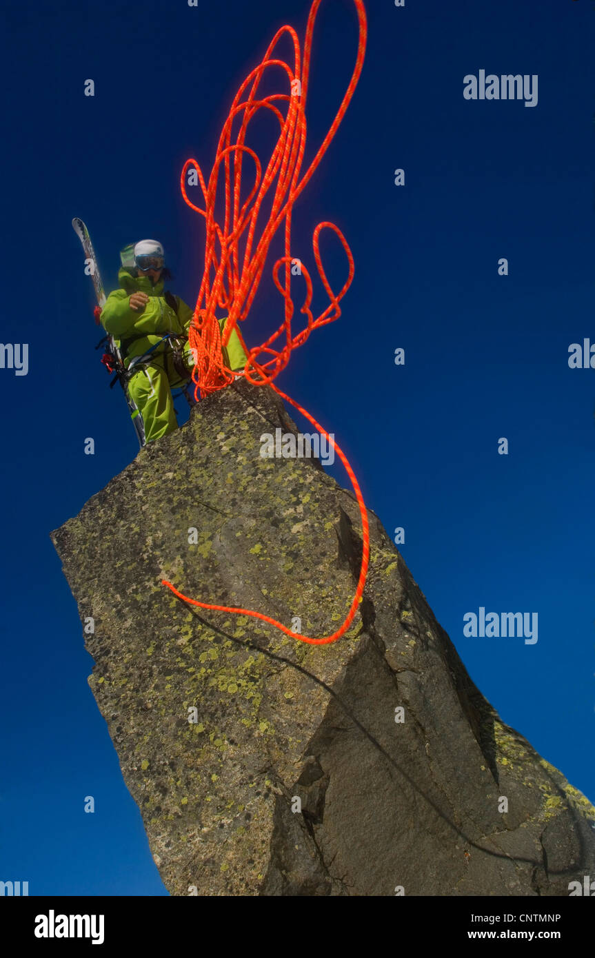 Alpinista di sci in piedi su una roccia e buttare giù un rosso corda di arrampicata, Francia, Alpi Foto Stock