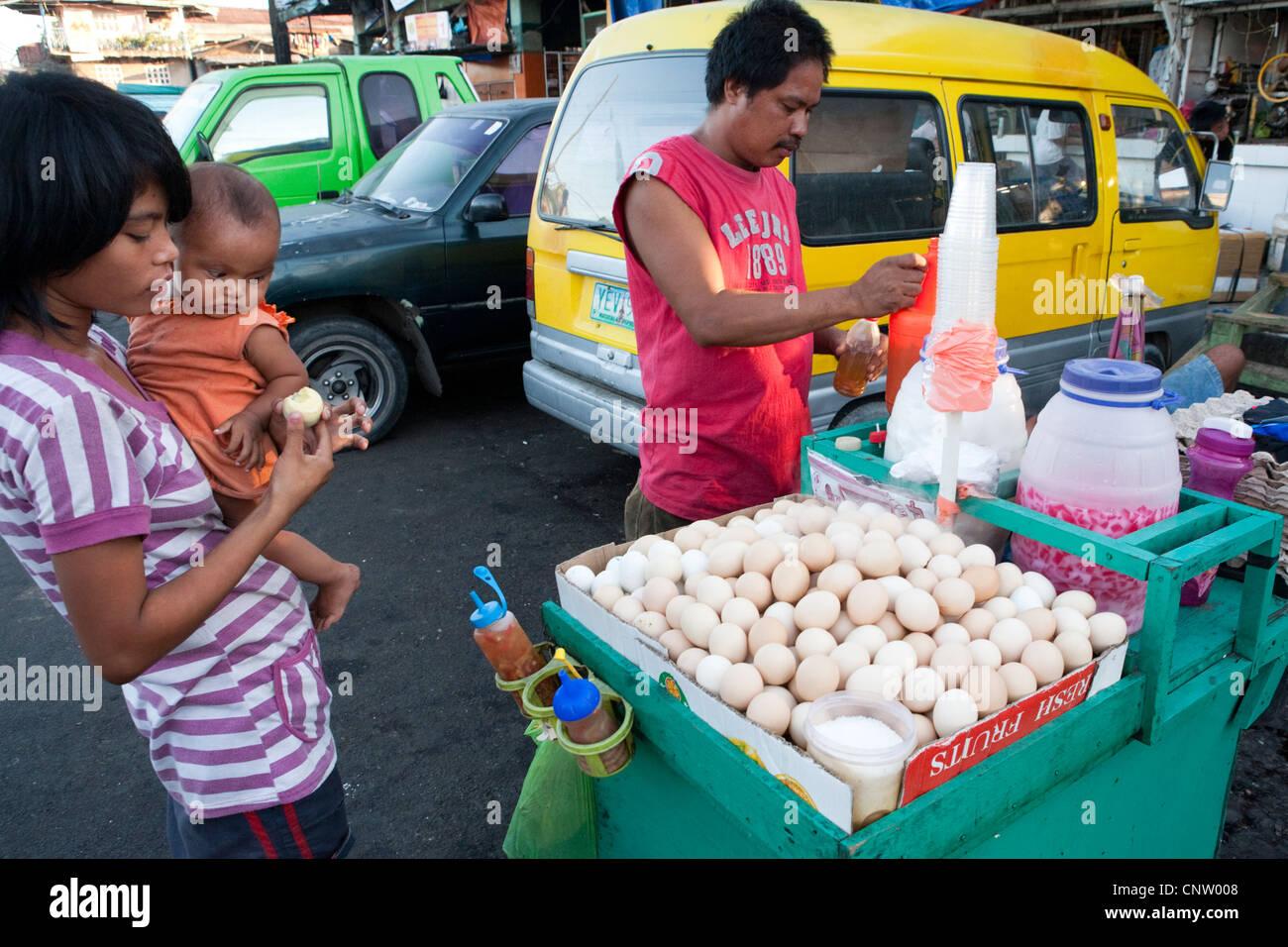 Donna con il suo bambino sta acquistando Balut, un anatra fecondate di embrioni da un fornitore sul ciglio della strada. Mercato del carbonio, Cebu City, Filippine Foto Stock