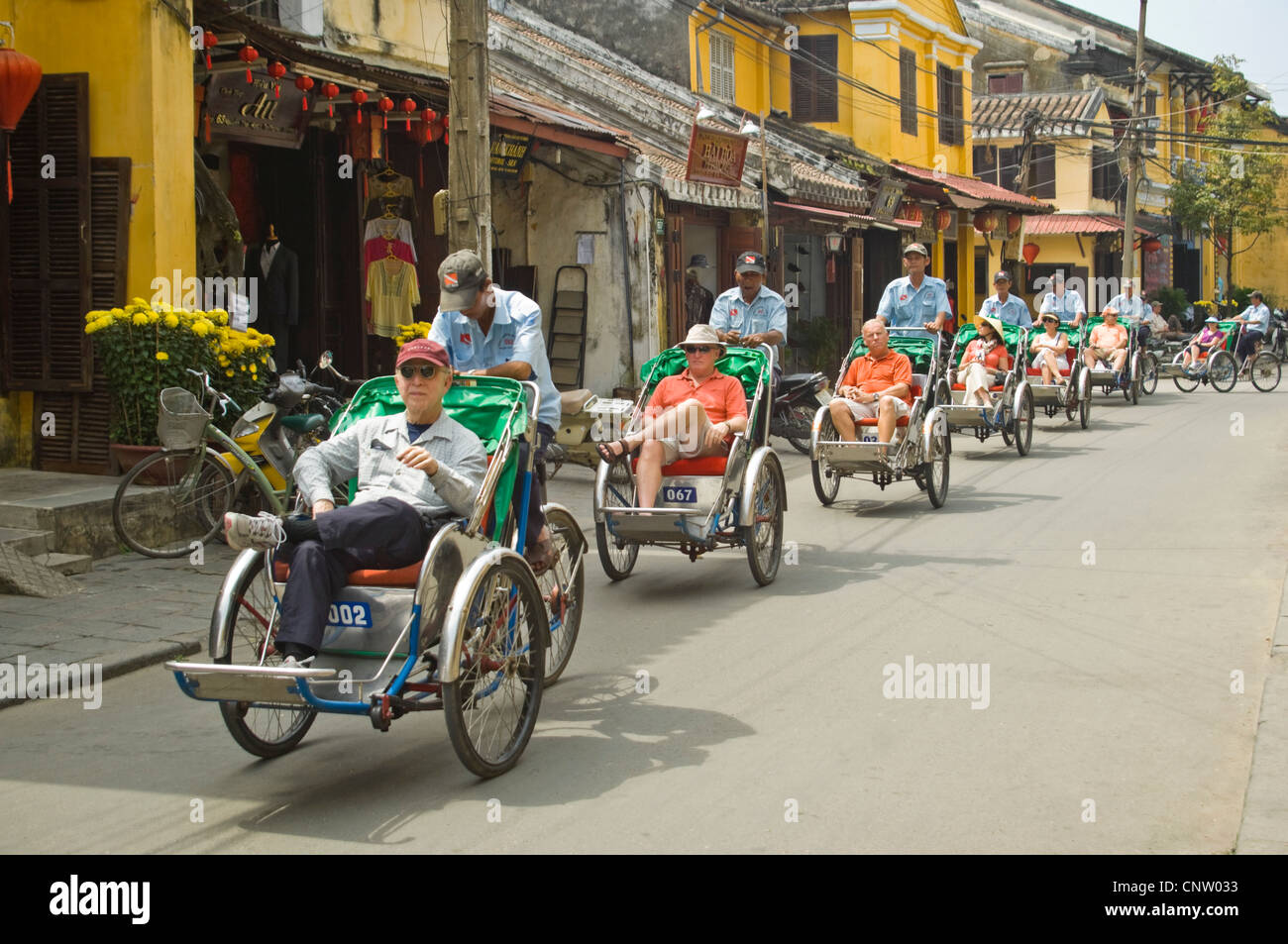 Orizzontale vista umoristico di turisti sul ciclo-rickshaws o cyclo cavalcando attraverso la antica città di Hoi An, Vietnam. Foto Stock