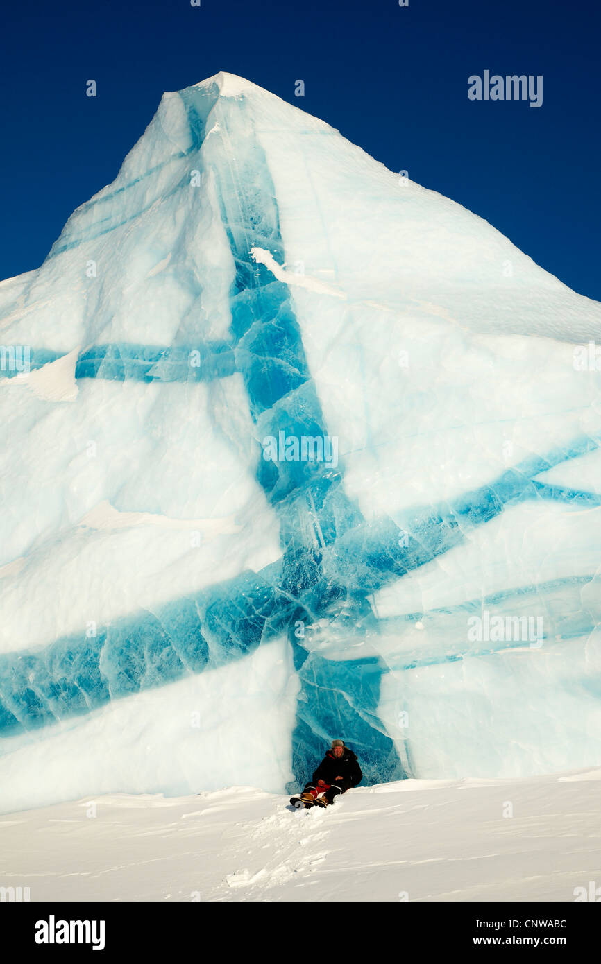 Uomo seduto nella neve davanti di iceberg con venature blu, Groenlandia, Ostgroenland, Tunu, Kalaallit Nunaat, Liverpool Land, Lillefjord Foto Stock