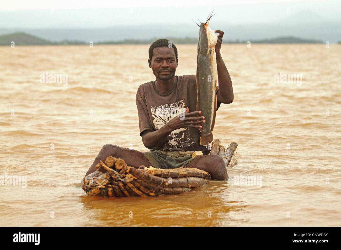 Pescatore in un lago che mostra prudly un pesce pescato, Kenya Mombasa Foto Stock