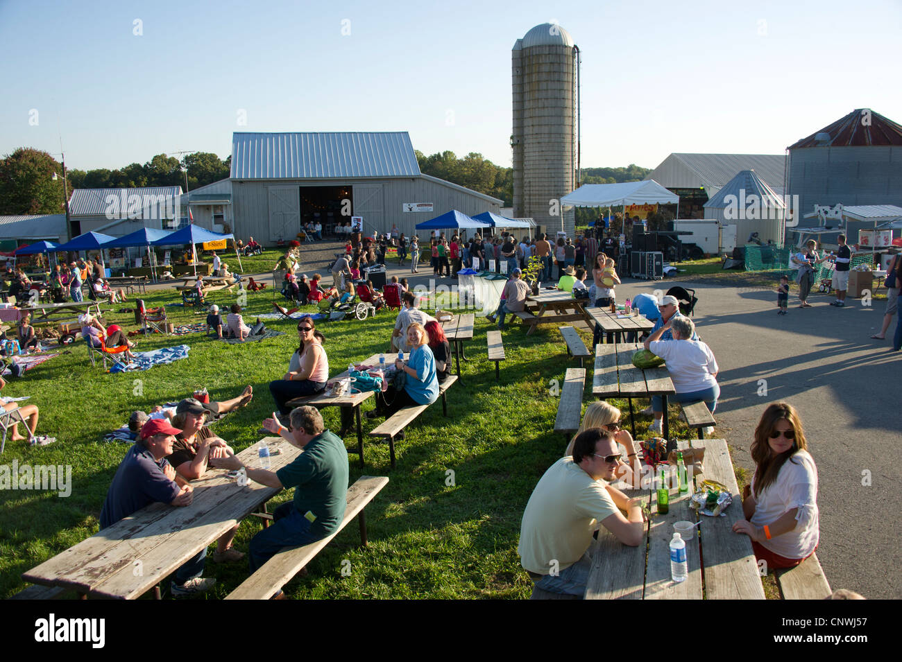 Festival con la folla a tavoli da picnic e oziare in erba in una fattoria Foto Stock