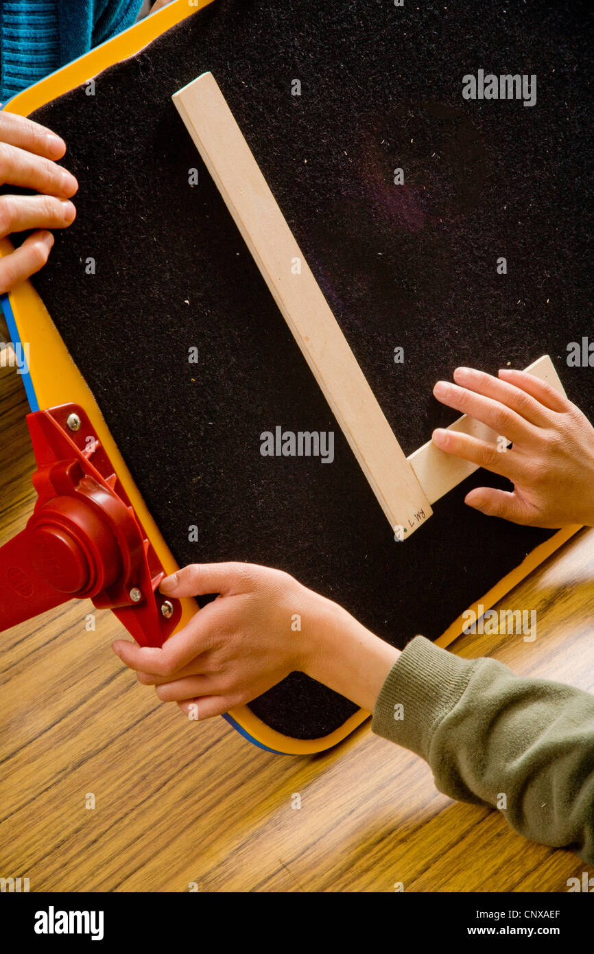 Un insegnante guida un bambino non vedente le mani per formare la lettera 'L' di touch utilizzando due bastoni in una speciale ha bisogno di pre-scrittura Braille c Foto Stock