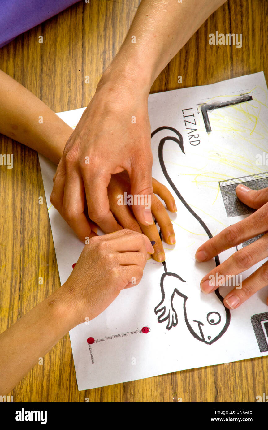 Un insegnante guida un bambino non vedente le mani sopra il contorno di una lucertola in rilievo in una speciale ha bisogno di scrittura di classe. Foto Stock
