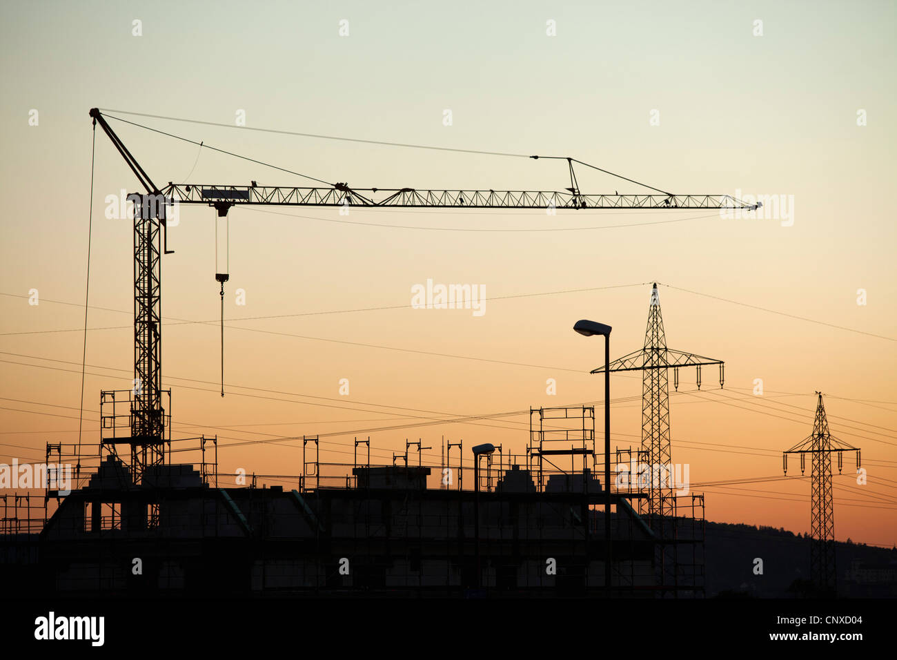 Una gru da cantiere e elettricità tralicci stagliano contro un Cielo di tramonto Foto Stock