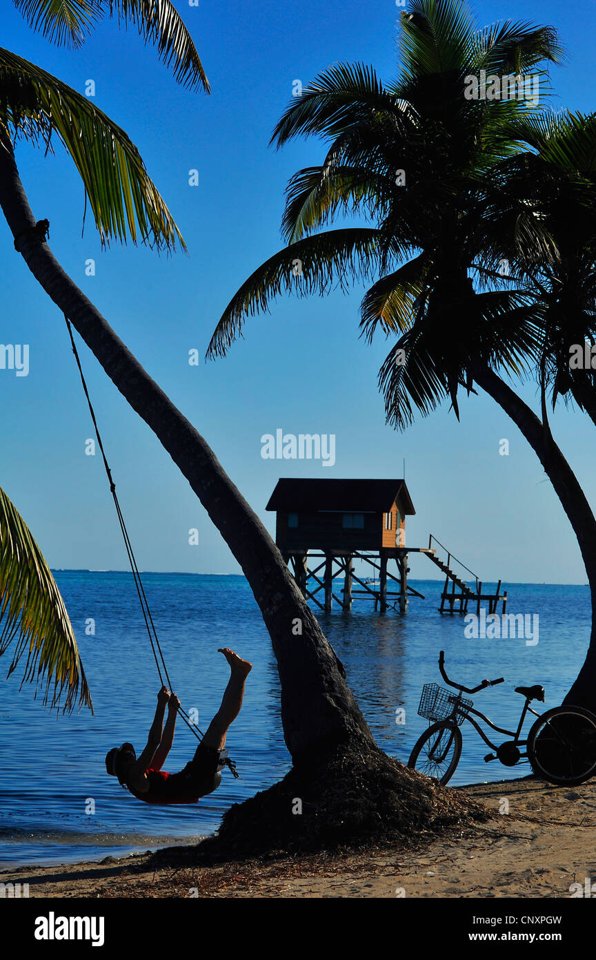 Silhouette di una persona dopo aver parcheggiato la sua bicicletta sulla sandbeach e swinnging su un altalena, Belize, isola di Ambergris Caye Foto Stock