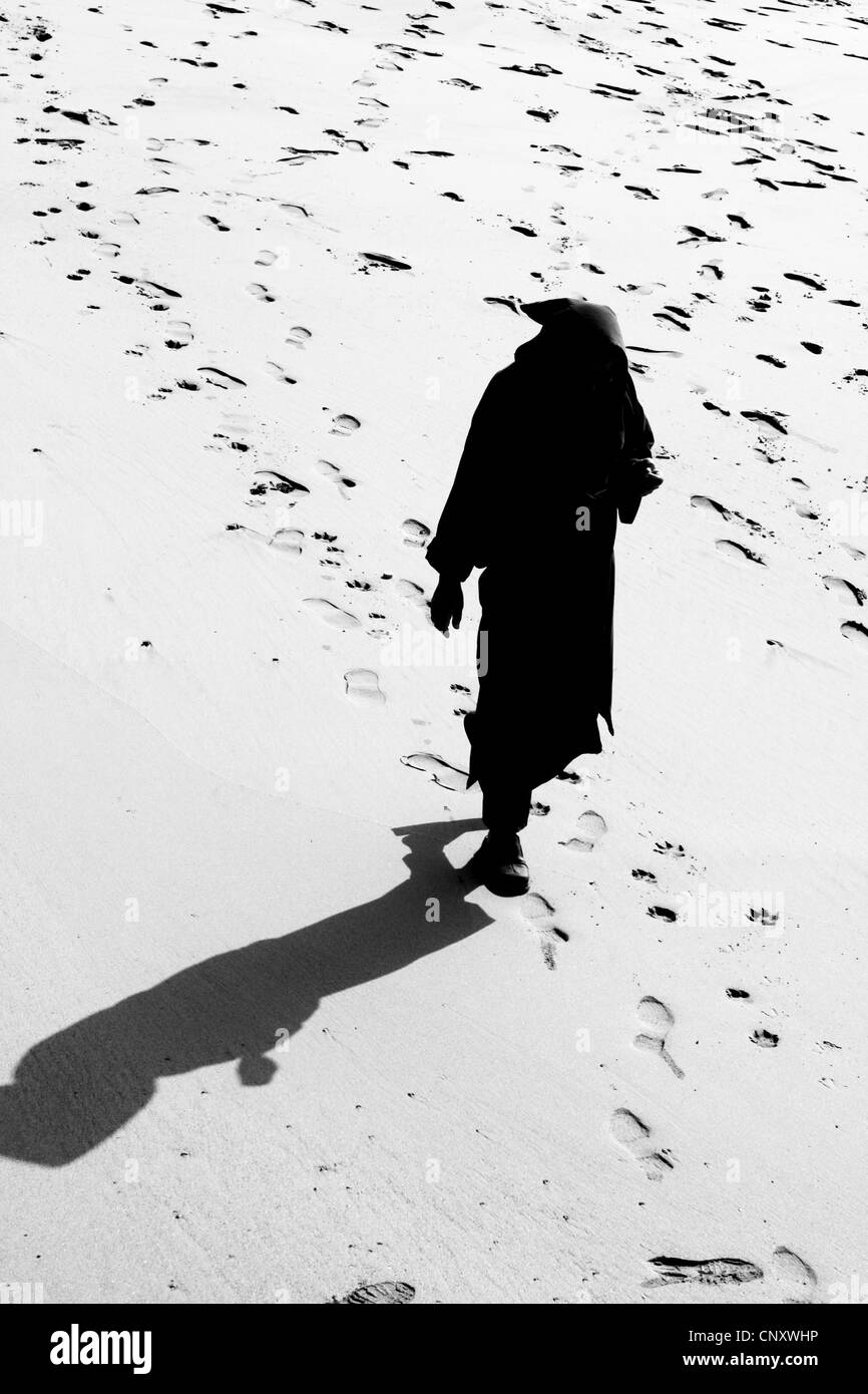 Silhouette e l'ombra del musulmano con cappuccio da uomo a camminare lungo la spiaggia in Marocco Foto Stock