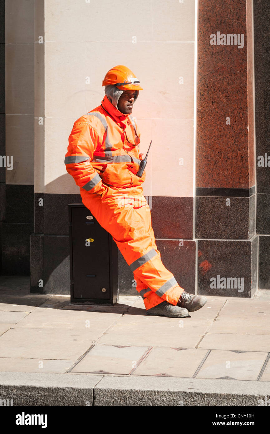 City of London etnica operaio britannico operaio in day glow tuta casco seduto nel sole di primavera a prendere il sole su metallo tfl scatola di giunzione Foto Stock