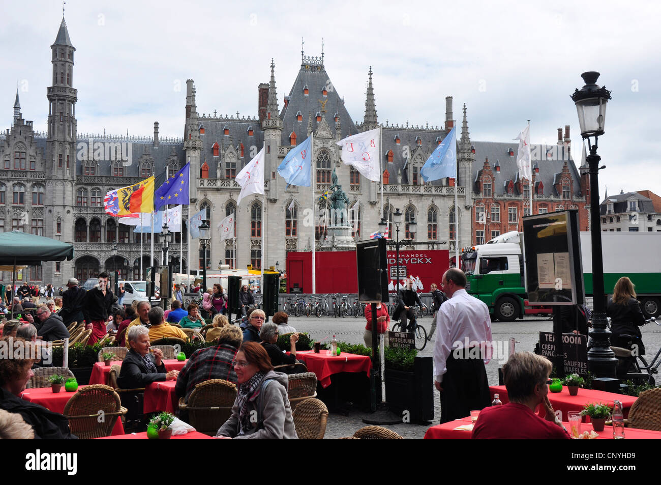 Belgio - Bruges - Piazza del Mercato - sfondo di antico municipio gotico - bandiere nazionali - la colorata vita ristorante Foto Stock