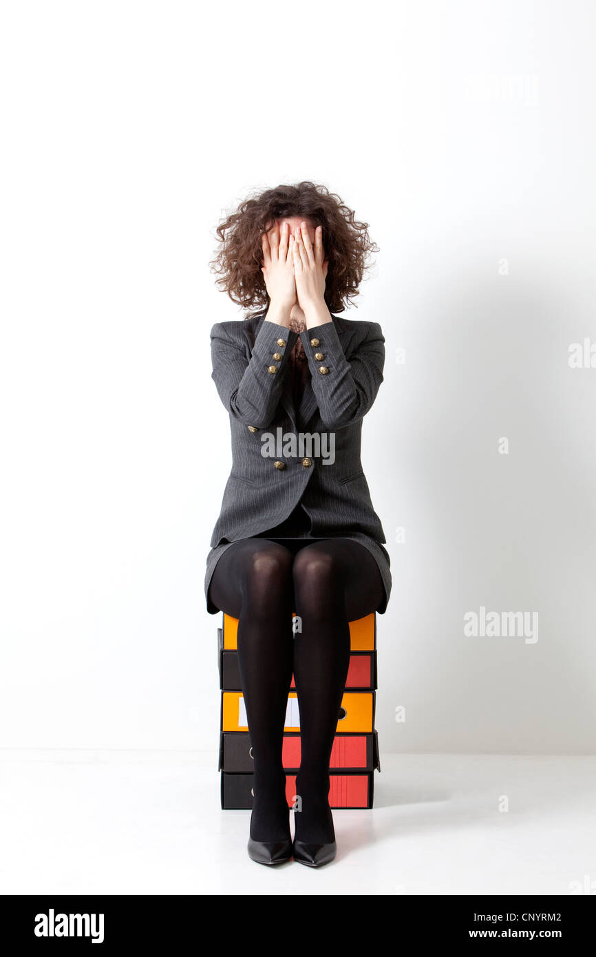 Una donna si copre la faccia mentre è seduto su contenitori per documenti Foto Stock