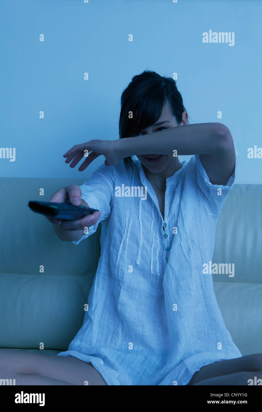 Spaventata donna che guarda la TV con un telecomando in mano Foto Stock