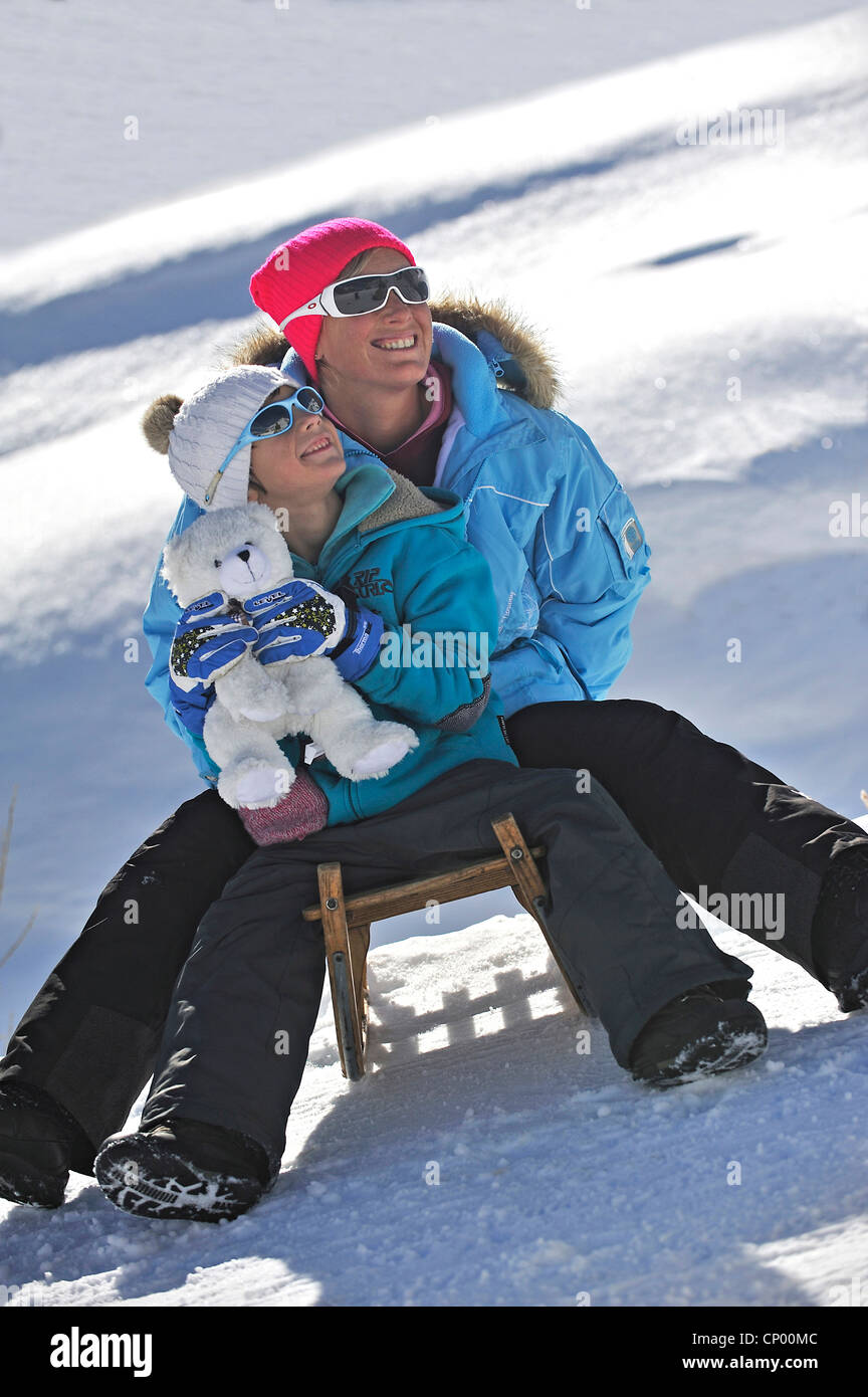 Madre e figlio sorridere mentre seduti insieme su una slitta a snowbound pendio di montagna, Francia Foto Stock