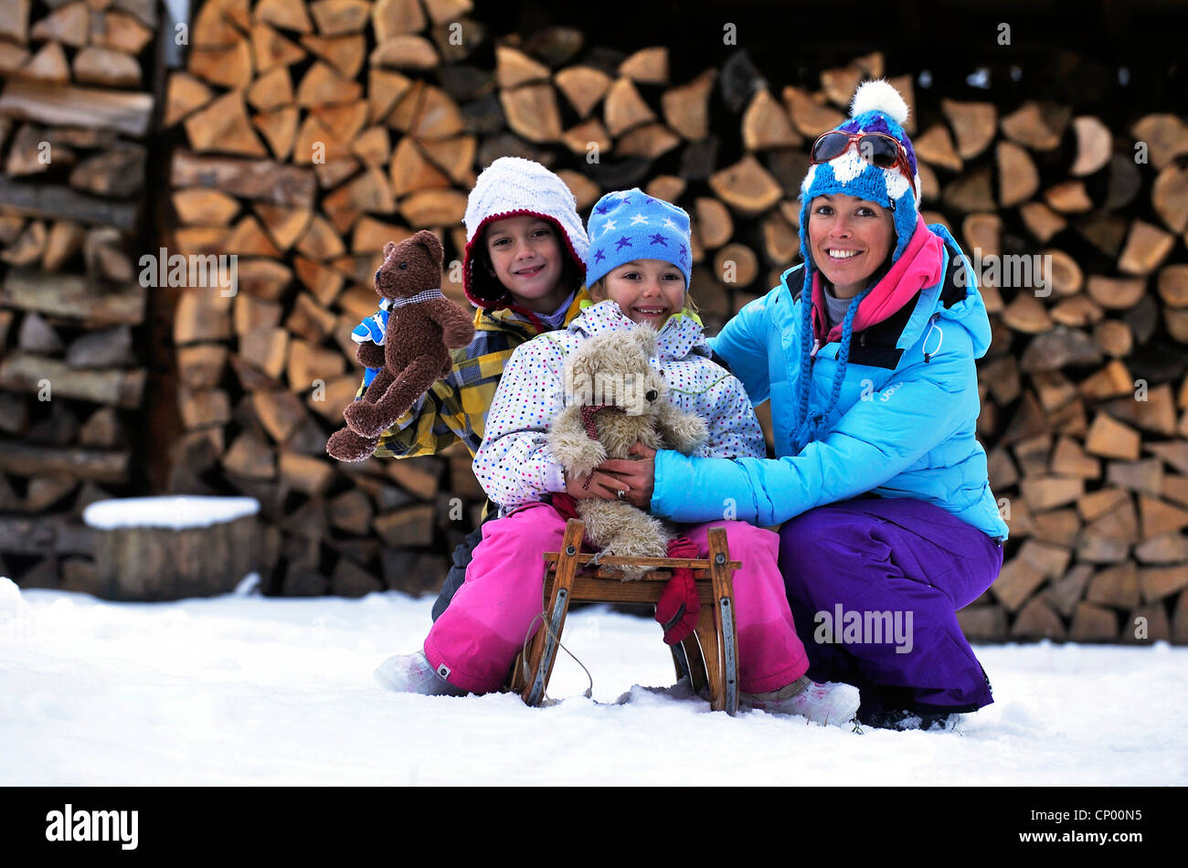 Madre accovacciato nella neve accanto ai suoi due figli seduto su di una slitta con la loro orsetti in mano, Francia Foto Stock