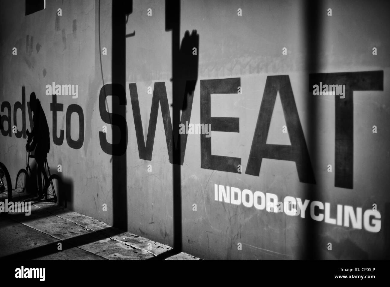 Foto in bianco e nero del ciclista ombra su un muro di un indoor cycling hall con la parola sudore sulla parete. Foto Stock