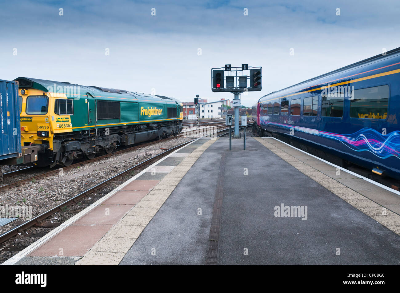 Una classe di Freightliner 66 locomotore voce un treno di contenitore carri merci, mentre un treno passeggeri foglie su un'altra linea. Foto Stock