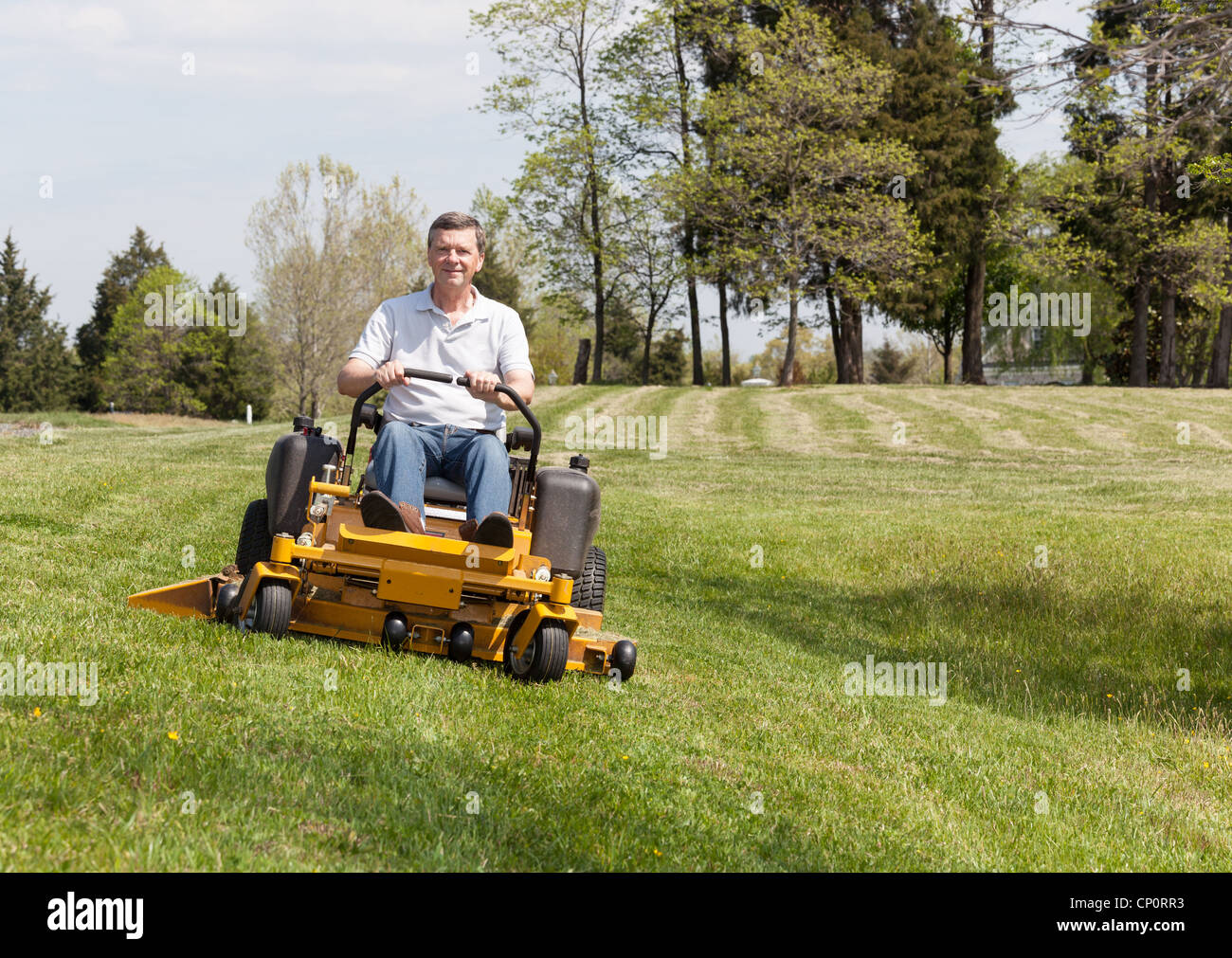 Senior pensionati maschio di falciare il prato e il taglio dell'erba su un grande prato con zero giallo-giro giro sul tosaerba Foto Stock