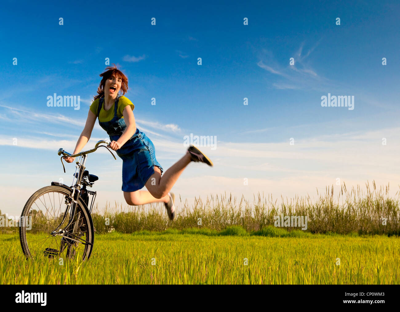 Donna felice con una vecchia bicicletta in un prato verde e salto Foto Stock