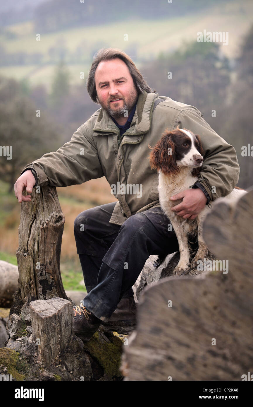 Una collina contadino con il suo cane spaniel su un albero caduto in Wales UK Foto Stock