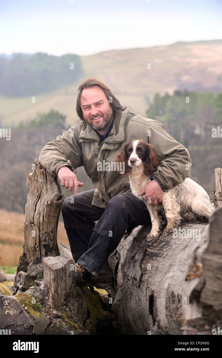Una collina contadino con il suo cane spaniel su un albero caduto in Wales UK Foto Stock