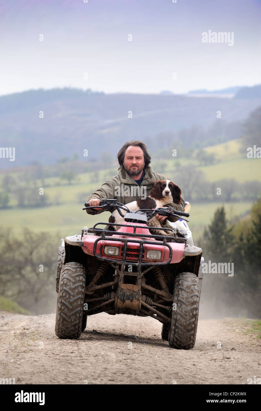 Un agricoltore su di una moto quad con il suo cane Spaniel Wales, Regno Unito Foto Stock