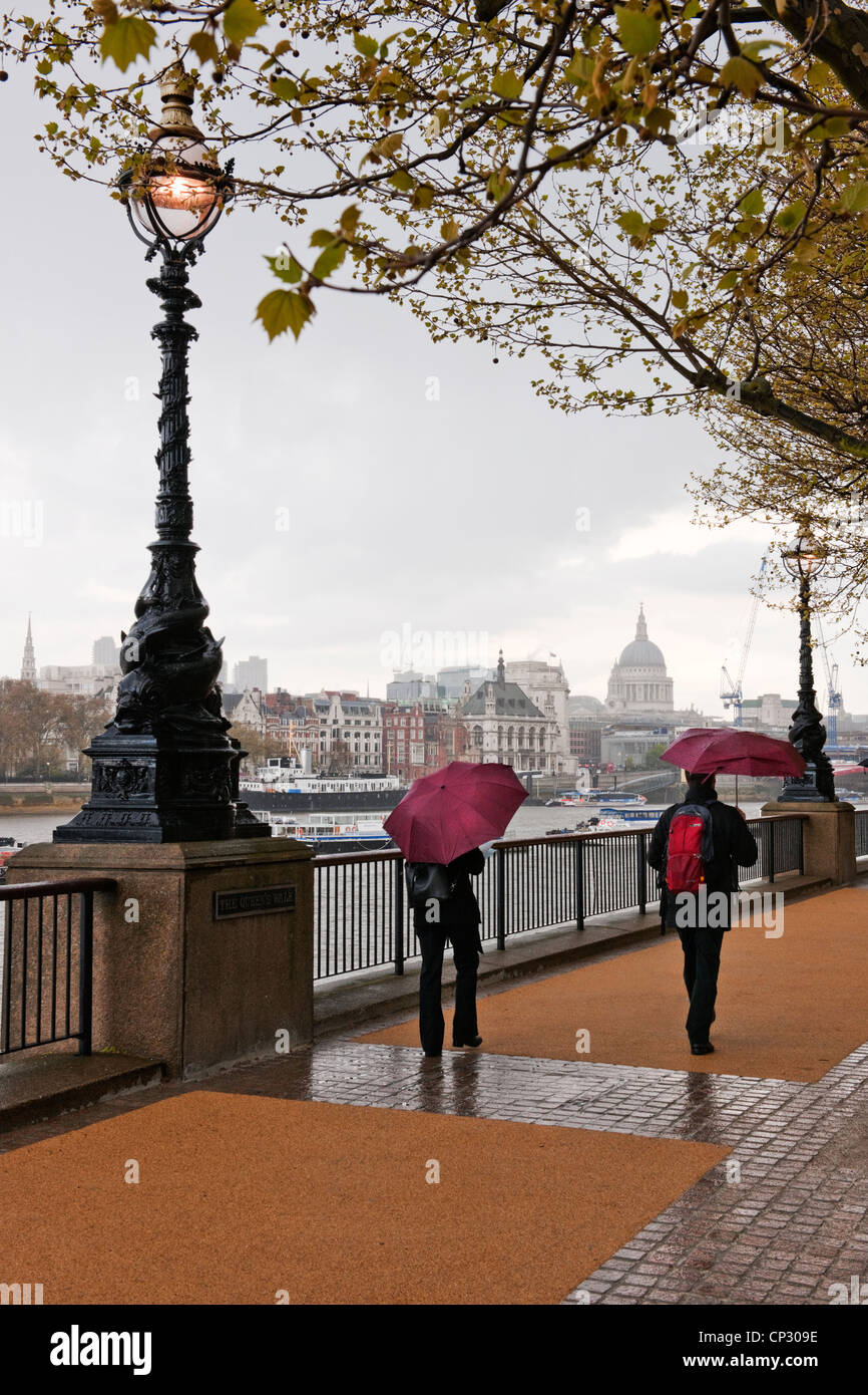 Due persone che camminano con ombrelloni su Queens a piedi South Bank in una molla doccia illuminata con luce in stile vittoriano e la Cattedrale di St Paul Foto Stock