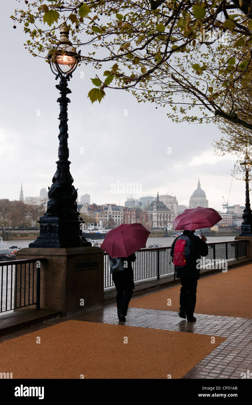 Due persone che camminano con ombrelloni su Queens a piedi South Bank in una molla doccia illuminata con luce in stile vittoriano e la Cattedrale di St Paul Foto Stock