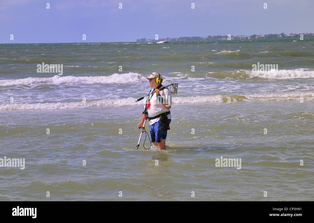 Armato di un rilevatore di metalli e di un filtro, un uomo cerca una spiaggia poco profonda area per il tesoro Foto Stock