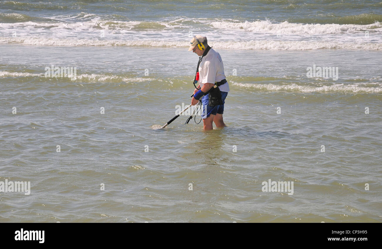 Armato di un rilevatore di metalli e di un filtro, un uomo cerca una spiaggia poco profonda area per il tesoro Foto Stock
