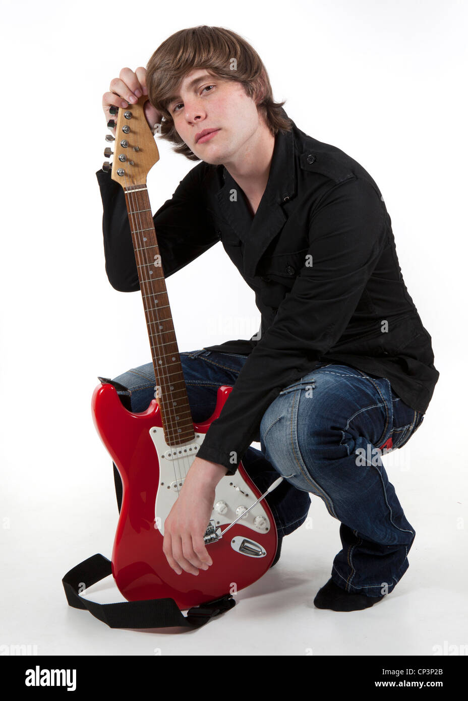 A lunghezza piena di colore studio ritratto di uomo che indossa jeans e maglietta scura accovacciato sul pavimento tenendo un rosso di chitarra elettrica Foto Stock