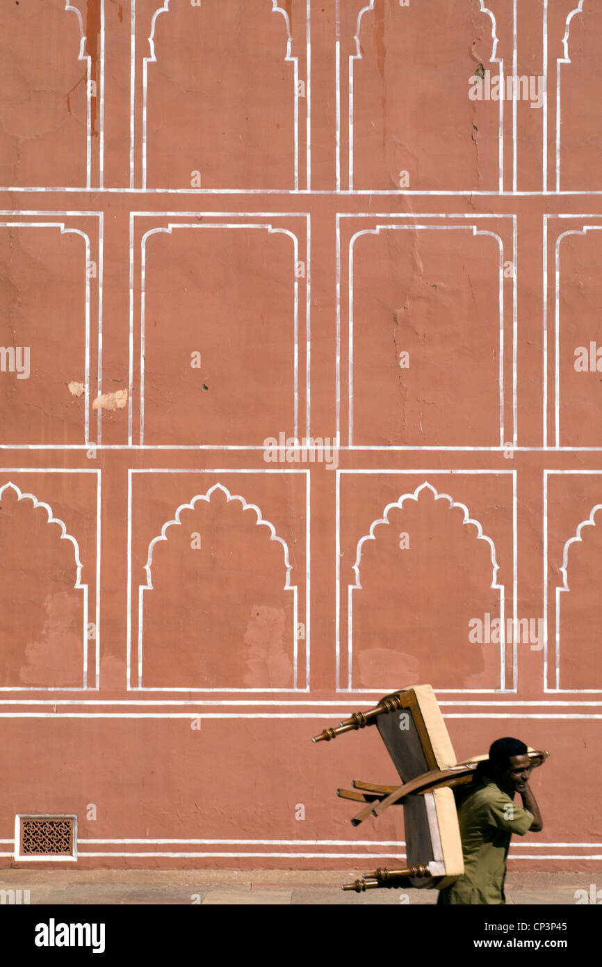 Un uomo porta due sedie oltre le pareti dipinte sul Palazzo di Città, Jaipur, India Foto Stock