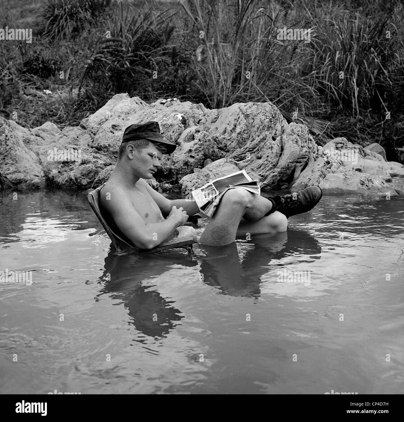 Guerra del Vietnam. US Marine rifleman prende il tempo per rilassarsi in un ambiente fresco ruscello di montagna, con una comoda sedia e il suo preferito Foto Stock