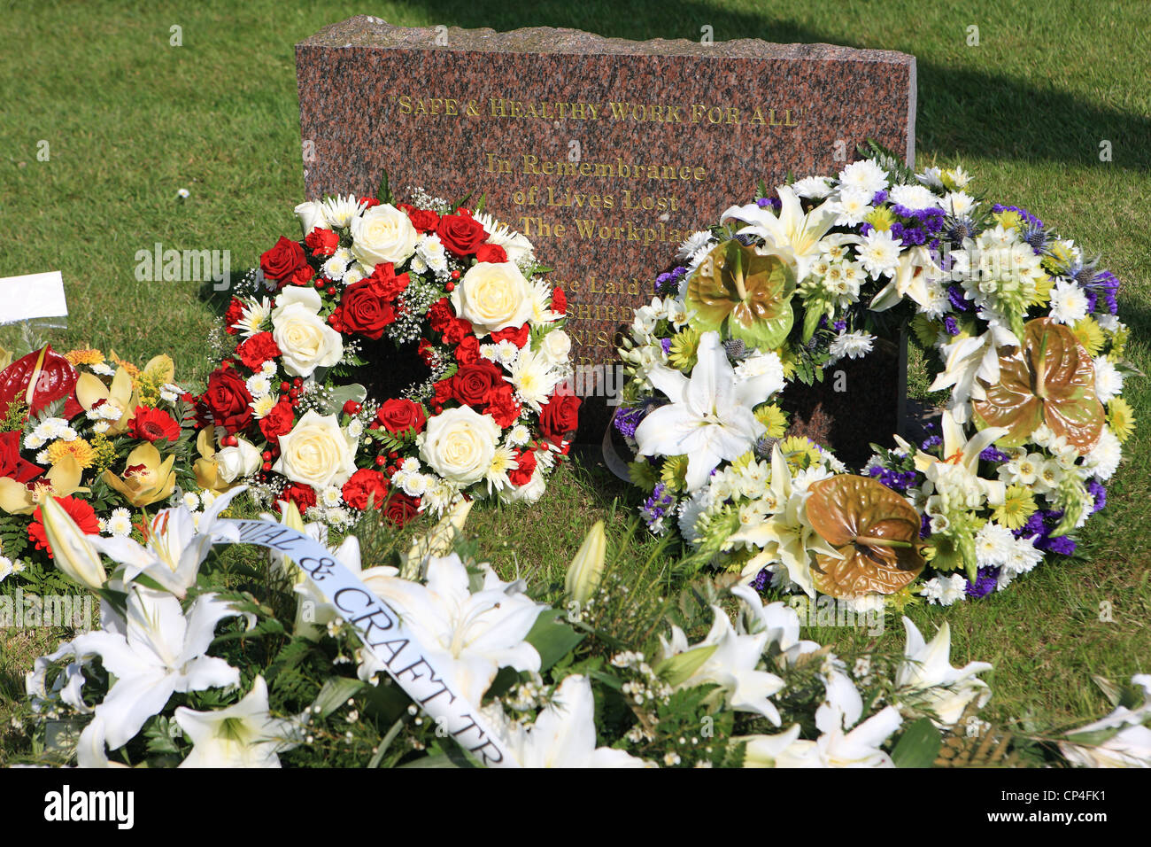 Ghirlande contro una lapide in memoria di vite perdute nel luogo di lavoro nel Renfrewshire città di Paisley in Scozia Foto Stock