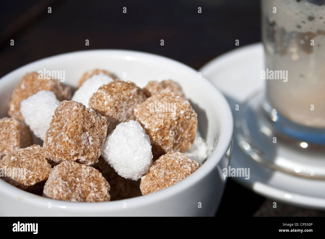 Zuccheriera con cubetti di marrone e bianco zucchero e un vuoto di latte vetro caffè. Foto Stock