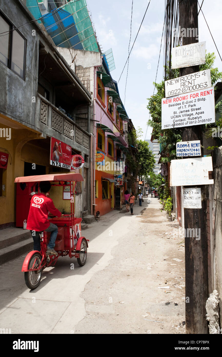 Camera in affitto dei manifesti in una strada laterale, fornitore di gelati in sella passato sul suo trisikad. Cebu City Cebu, Visayas nelle Filippine. Foto Stock