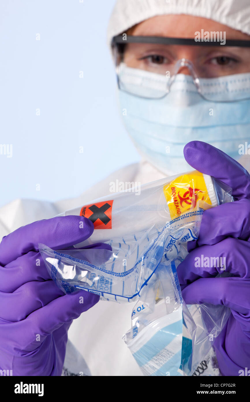 Foto di un laboratorio forense tecnico di indumenti da lavoro protettiva esaminando un contenitore in plastica che è bianco in polvere Foto Stock