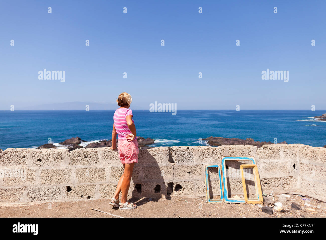 La donna in rosa di t-shirt e pantaloncini corti che guarda al mare con il cielo limpido da Tenerife, La Gomera all'orizzonte, Isole Canarie Foto Stock