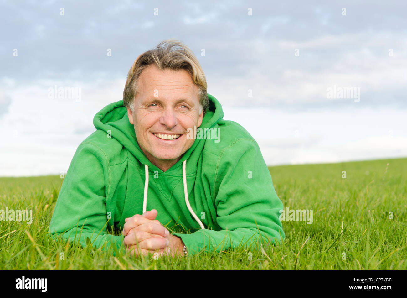 Un ritratto di un sorridenti bionda uomo sulla quarantina che indossa un top verde e posa su erba verde. Foto Stock