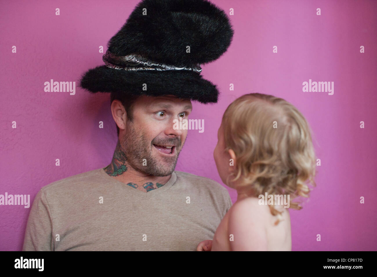 Tatuato papà facendo una buffa faccia per sua figlia a casa e mettere su un cappello spiritoso. Foto Stock