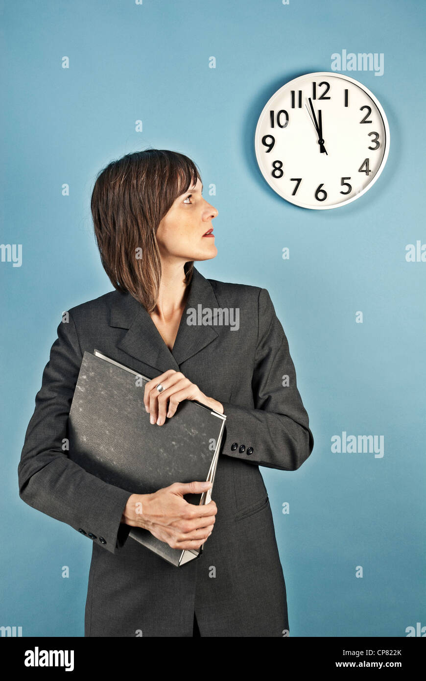 Imprenditrice guardando un orologio da parete. Si tratta di quasi dodici ore tempo di alta. Foto Stock