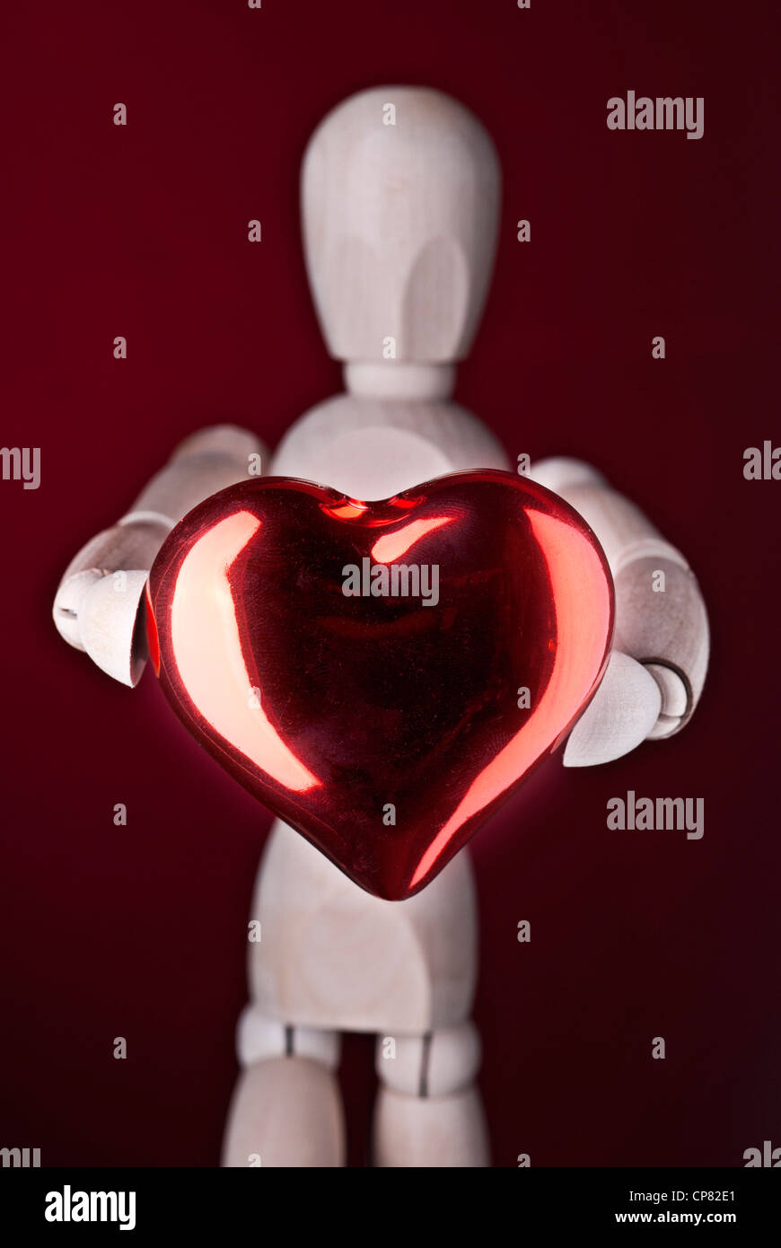 Un burattino di legno sorregge un cuore rosso, simbolo dell'amore. Foto Stock