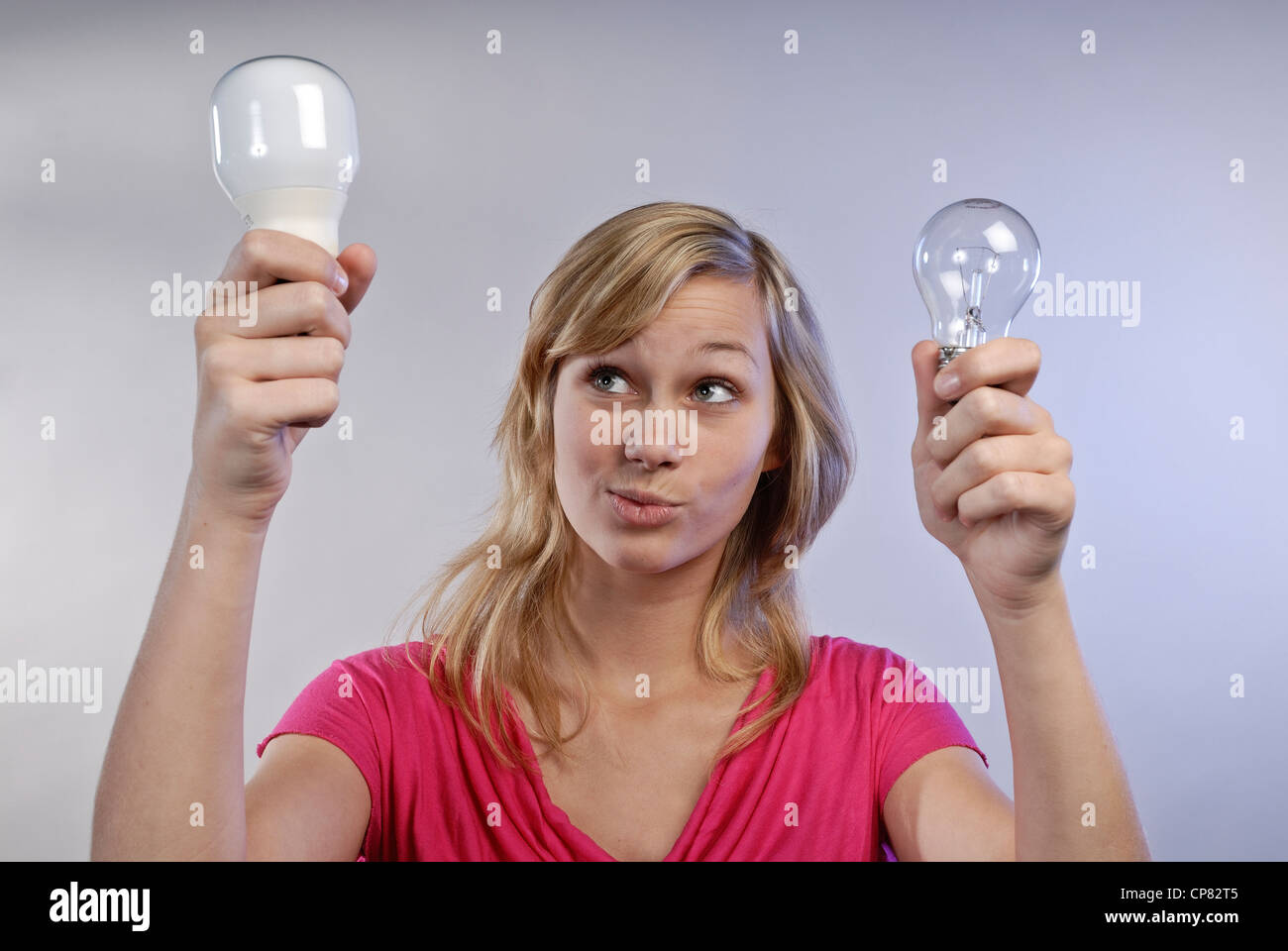 Giovane donna in possesso di un risparmio energetico lampada e una convenzionale lampadina della luce nelle sue mani. Guarda scettico. Foto Stock