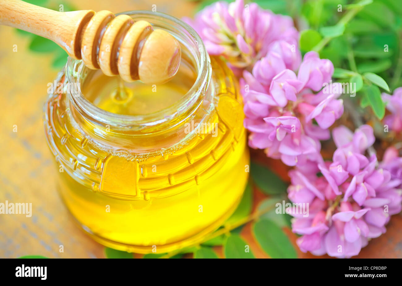 Il vasetto di vetro pieno di miele e stick con acacia fiori rosa e bianchi Foto Stock