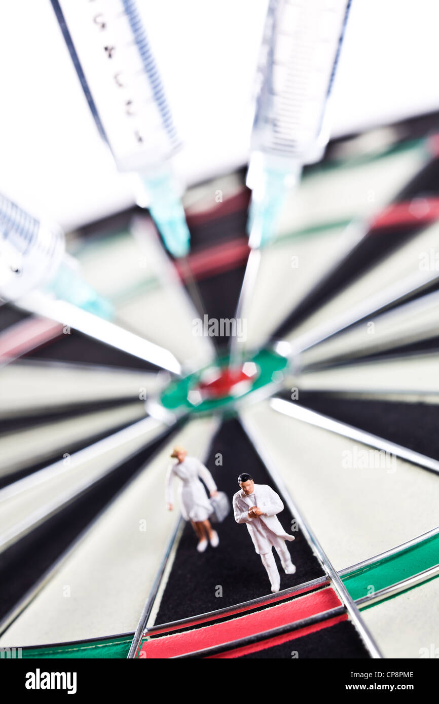 Siringhe bloccato in un dartboard con figure mediche Foto Stock