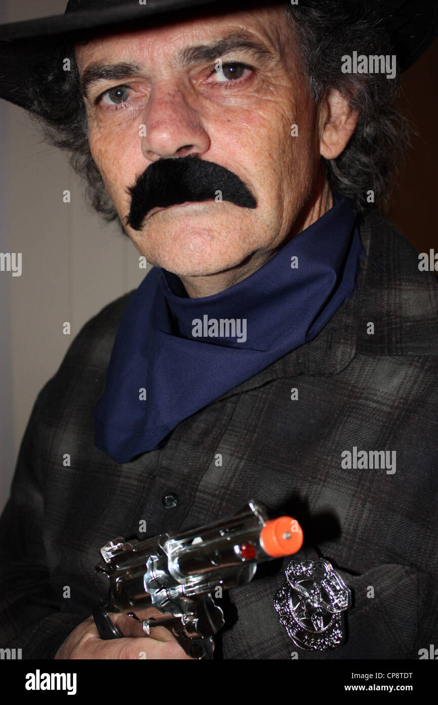 A cinquanta anni di vecchio uomo vestito da cowboy per una festa in costume verticale di sfondo semplice BDA Foto Stock