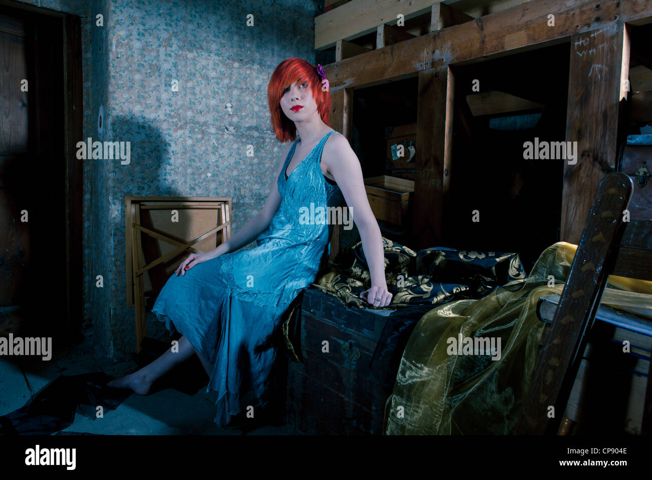 Un attraente giovane donna che indossa un blu abito in seta seduto da solo in un attico Foto Stock